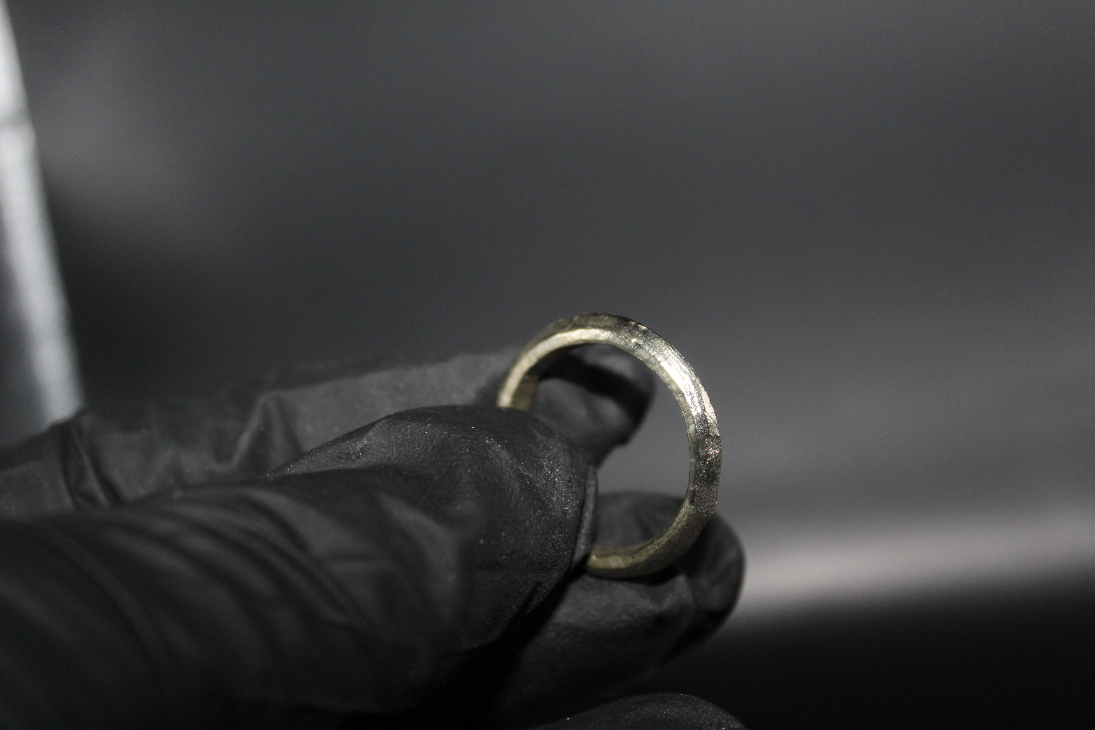 Hand wearing a black glove holding a tarnished silver ring against a dark background