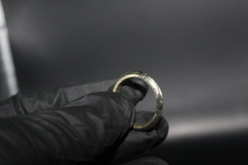 Hand wearing a black glove holding a tarnished silver ring against a dark background